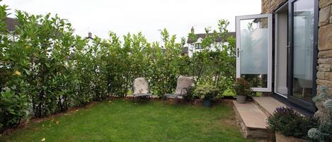 A well-maintained garden with a lawn, two chairs, and a stone wall.