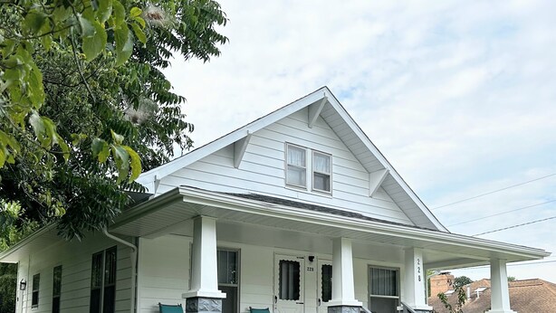 Ein zweistöckiges Haus mit Veranda, zwei Stühlen und einer Steinpfeiler.