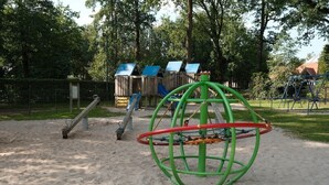 A playground with a seesaw, a climbing structure, and a green spherical climbing frame. - Familyfriendly house for 12 persons (Kasterlee)
