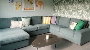 A modern living room with a sectional sofa, a marble coffee table, and a tropical leaf-patterned wallpaper. - Familyfriendly house for 12 persons (Kasterlee)