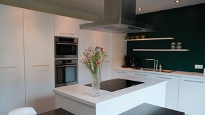 A modern kitchen with white cabinetry, a central island, a stainless steel range hood, and a vase with flowers. - Familyfriendly house for 12 persons (Kasterlee)