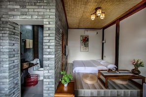 A compact room with a bed, a small table, and a wall-mounted shelf.