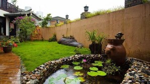 A garden with a pond, potted plants, and a traditional-style building.