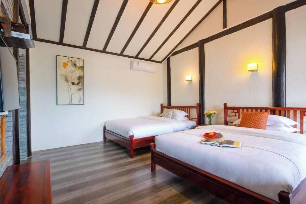 A hotel room with two wooden beds, a brick wall, and a ceiling with exposed beams.
