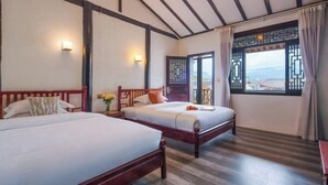 A hotel room with two beds, wooden beams on the ceiling, a large window with curtains, and wall-mounted lights.