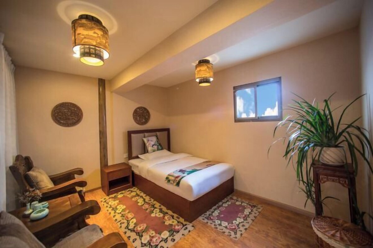 A bedroom with a bed, nightstand, wooden bench, and a potted plant.