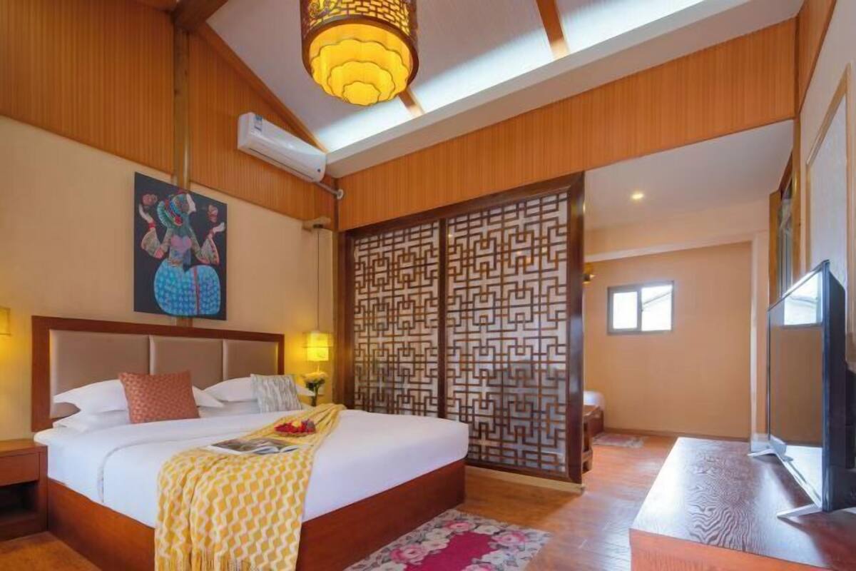 A bedroom with a large bed, wooden ceiling, decorative wall panel, and a television.