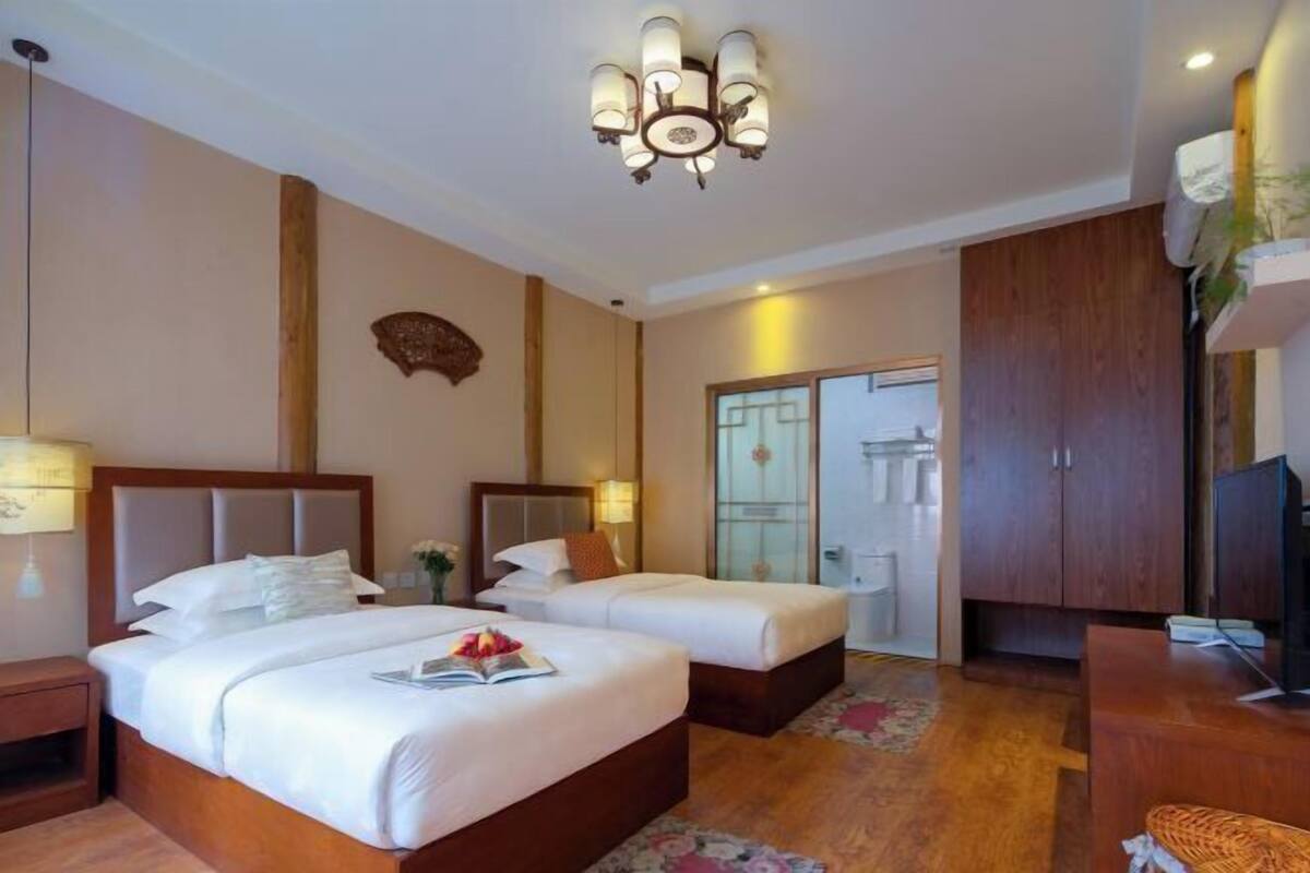 A hotel room with two beds, a wooden wardrobe, a television, and a chandelier.