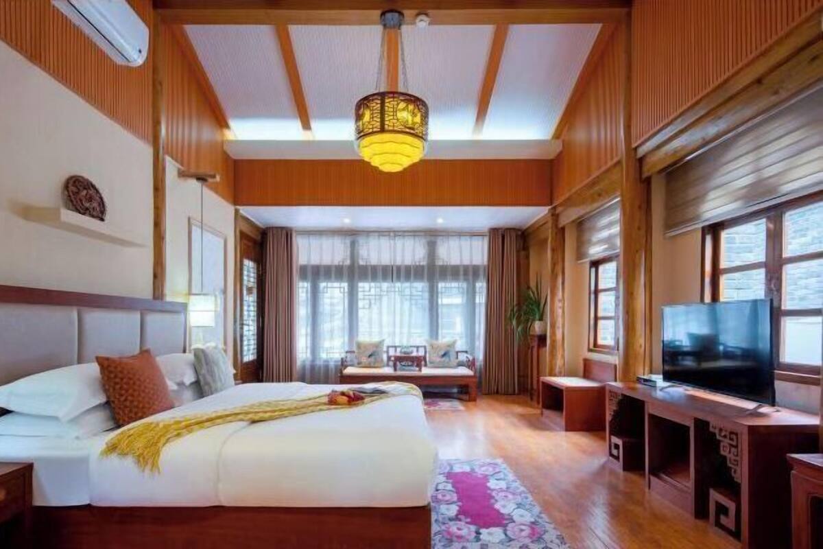 A spacious hotel room with a large bed, a television, a seating area, and a view of the outdoors.