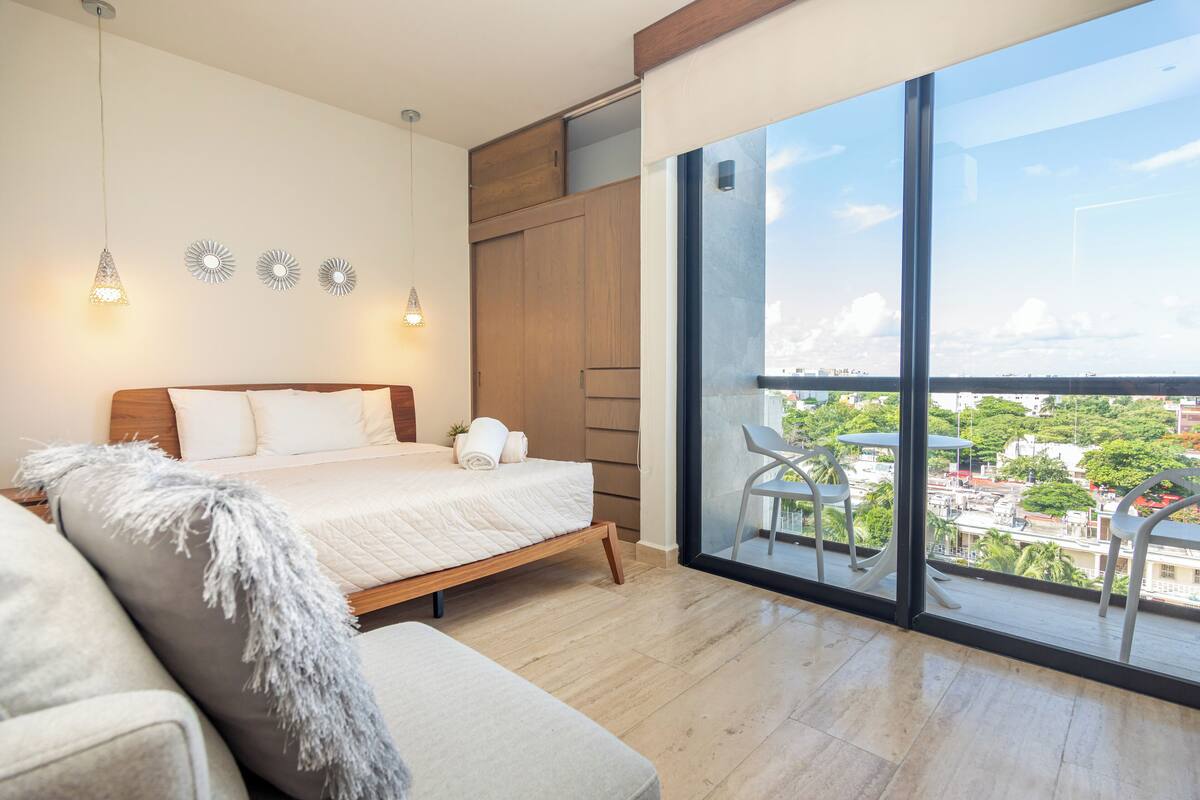 Ein Schlafzimmer mit einem großen Bett, einem Sofa, einem Balkon mit Blick auf die Stadt und dekorativer Wandkunst.