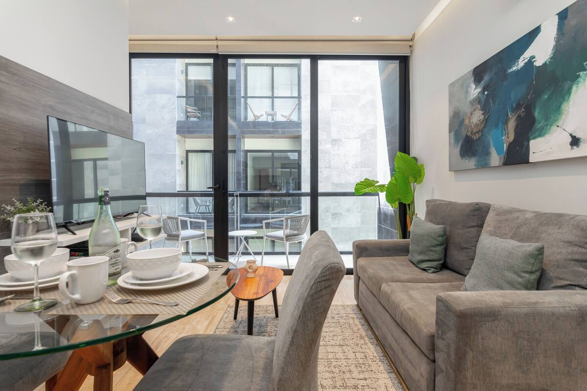 Ein modernes Wohnzimmer mit einem Glastisch, grauem Sofa und einem großen abstrakten Gemälde.