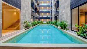 A modern indoor swimming pool with a central staircase and surrounding balconies. - Musa del Carmen By BoutiqueApartments MX (Playa del Carmen)