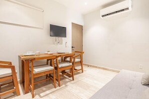 A small, well-lit room with a wooden dining table and chairs, a flat-screen TV mounted on the wall, and a ceiling air conditioner. - Musa del Carmen By BoutiqueApartments MX (Playa del Carmen)