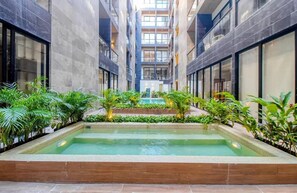 A modern indoor pool area with a central pool, surrounded by greenery and flanked by tall buildings. - Musa del Carmen By BoutiqueApartments MX (Playa del Carmen)