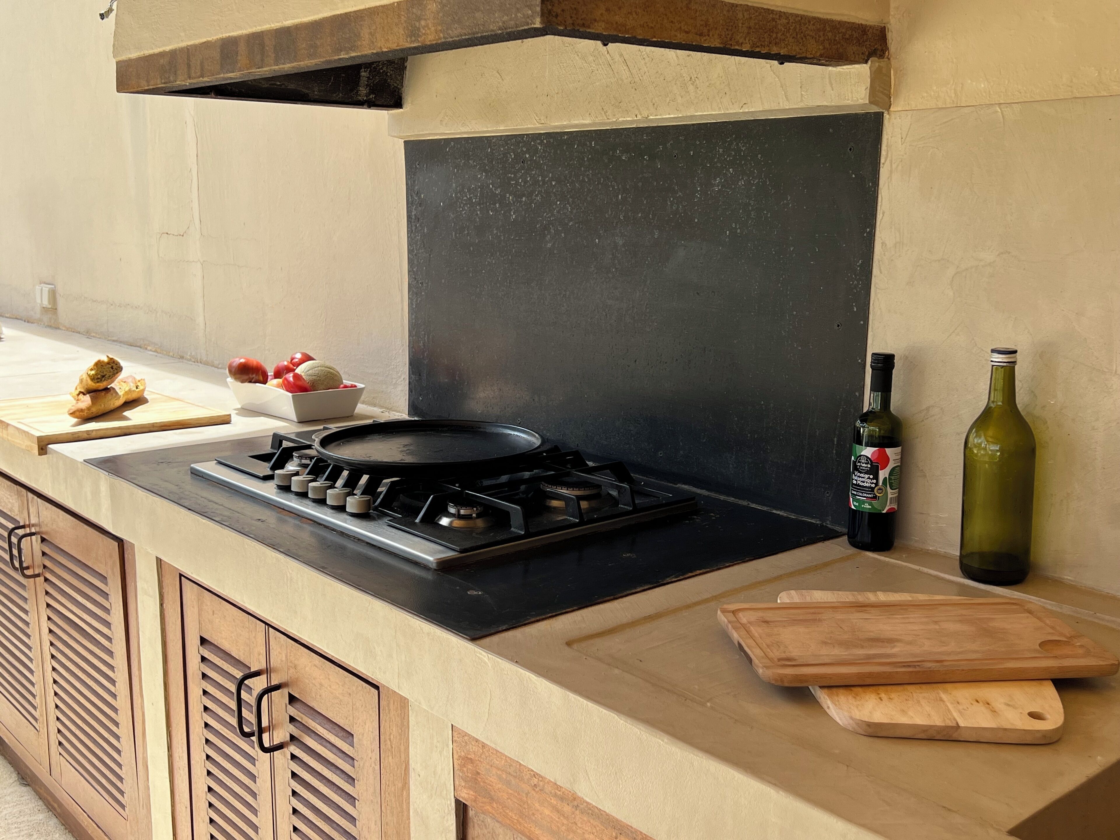 A kitchen with a gas stove, wooden cabinets, a cutting board, and a wine bottle.
