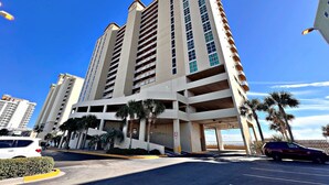 A multi-story hotel with a modern design, featuring a parking garage and palm trees in the foreground. - Crystal Shores West 707 (Gulf Shores)
