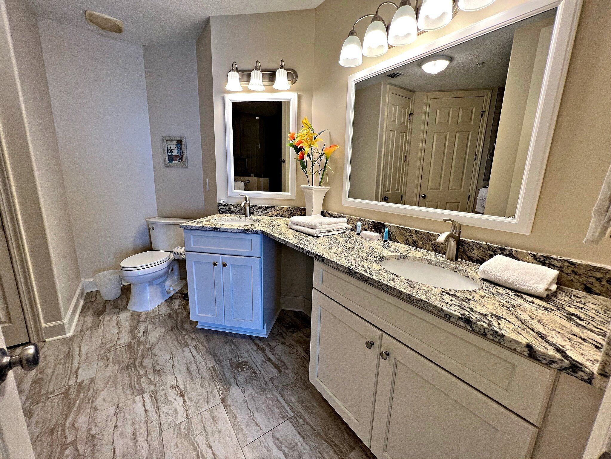 A bathroom with a marble floor, a sink with a large mirror, a toilet, and a vanity with cabinets.