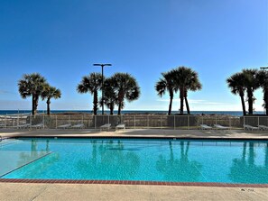 A swimming pool with a view of the ocean and palm trees. - Regency Isle 704 (Orange Beach)