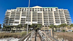 Un hôtel à plusieurs étages doté de balcons, une promenade en bord de mer et des palmiers.