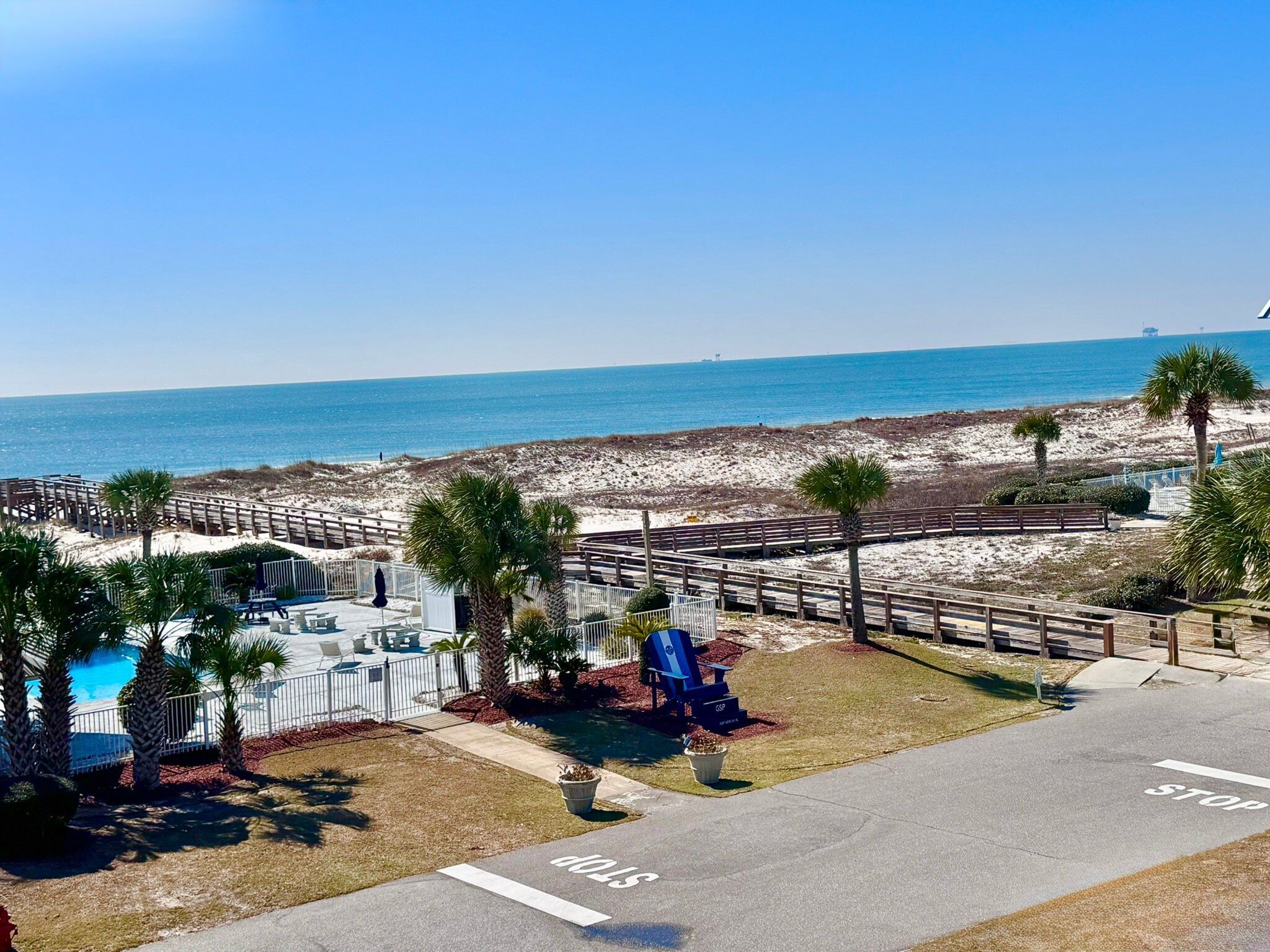 A beachside view with a clear sky, a sandy beach, and a wooden boardwalk leading to a pool area.