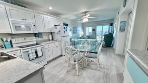 A modern kitchen with white cabinets, a dining area with a glass table and white chairs, and a ceiling fan.