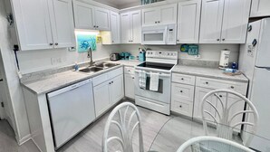 A modern kitchen with white cabinets, a built-in microwave, and a stove. There is a sink with a faucet, and a chair is visible in the foreground.