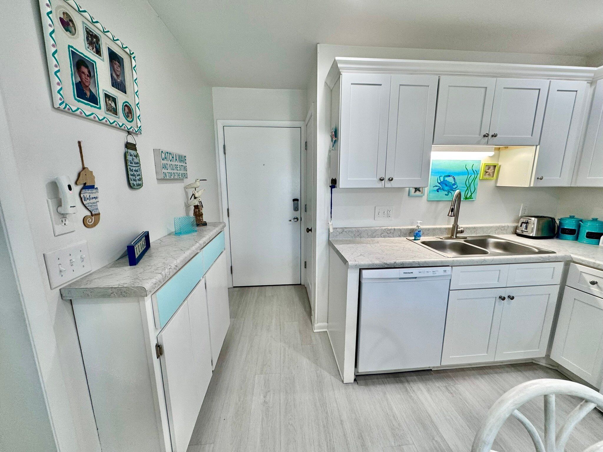 A compact kitchen with white cabinets, a built-in dishwasher, and a sink. There are decorative items on the wall and a small countertop with a toaster.