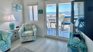 A living room with a view of the beach, a sofa, a chair, a lamp, and a TV.