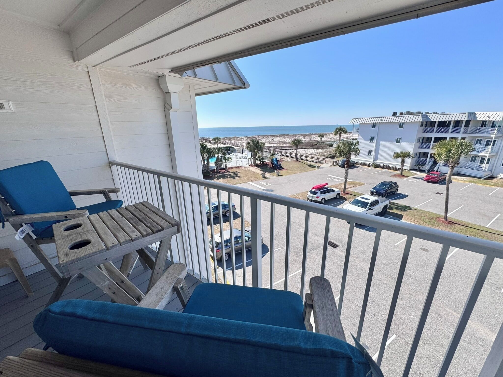 A balcony with blue chairs and a view of a parking lot and buildings.