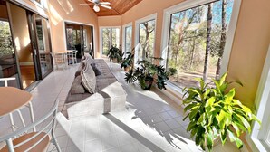 A spacious living area with a large sofa, a dining table, and multiple windows offering views of the outdoors. - Daphne River Villa (Daphne)
