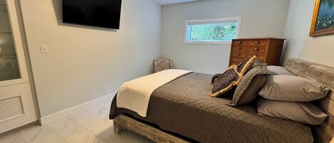 A bedroom with a bed, a ceiling fan, a TV, a window, and a dresser.