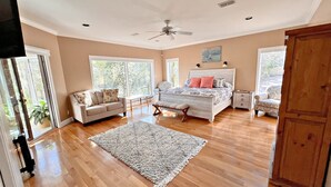 A spacious bedroom with a large bed, a sitting area with a sofa, and a view of the outdoors through large windows. - Daphne River Villa (Daphne)