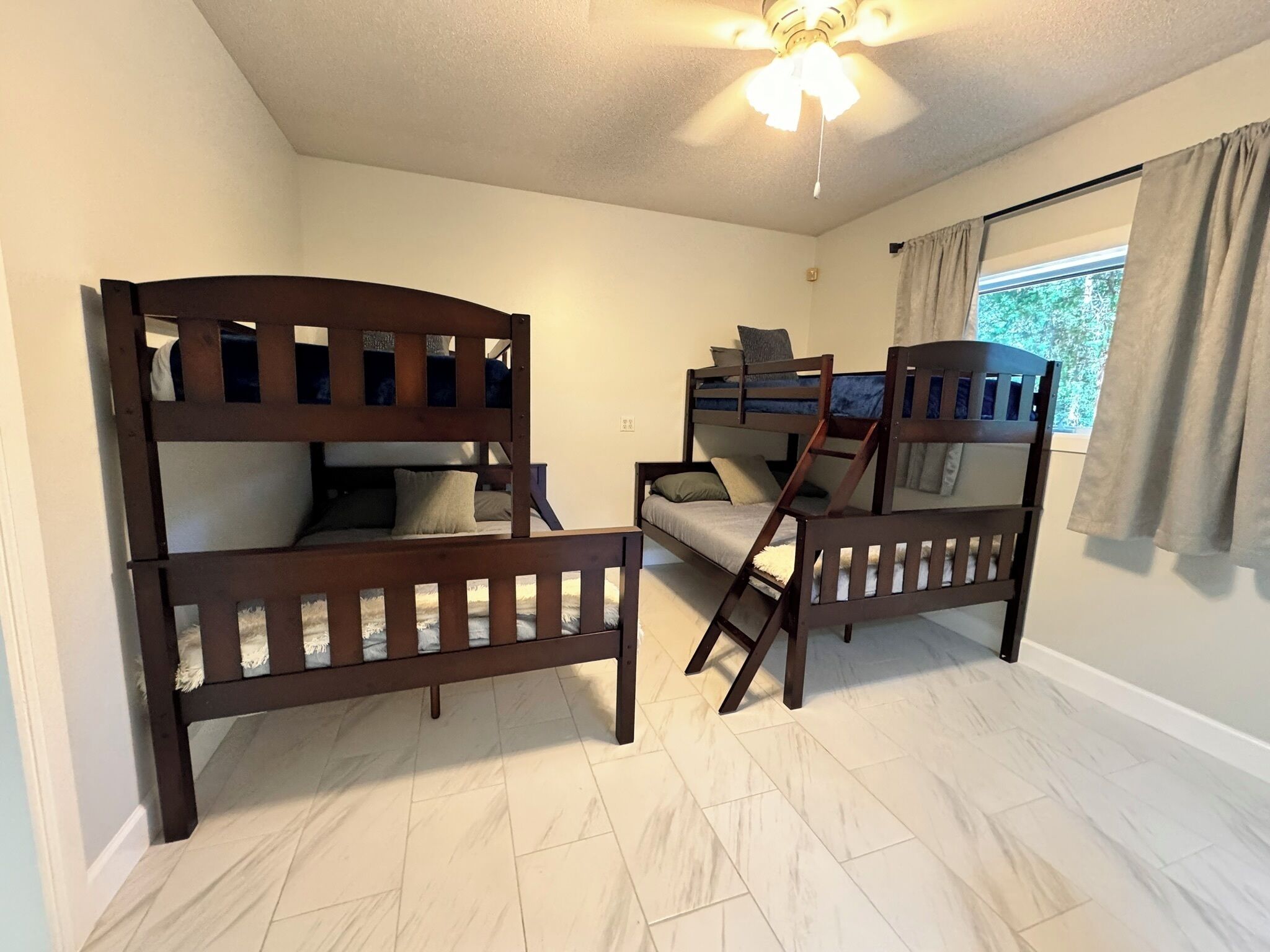 A room with two bunk beds, a ceiling fan, and a window with curtains.