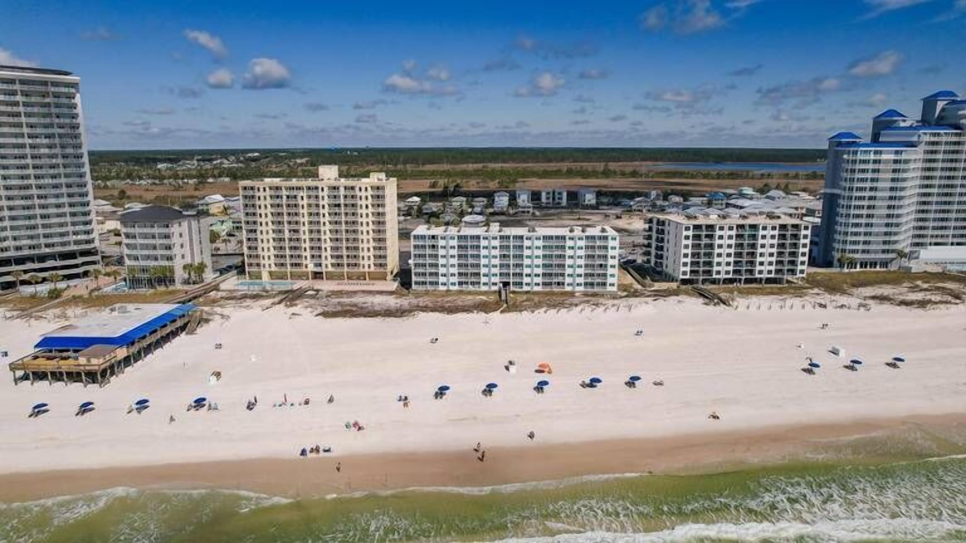 Ein Strandhotel mit mehreren Hochhäusern, einem Sandstrand und einer Pier mit Sonnenschirmen.
