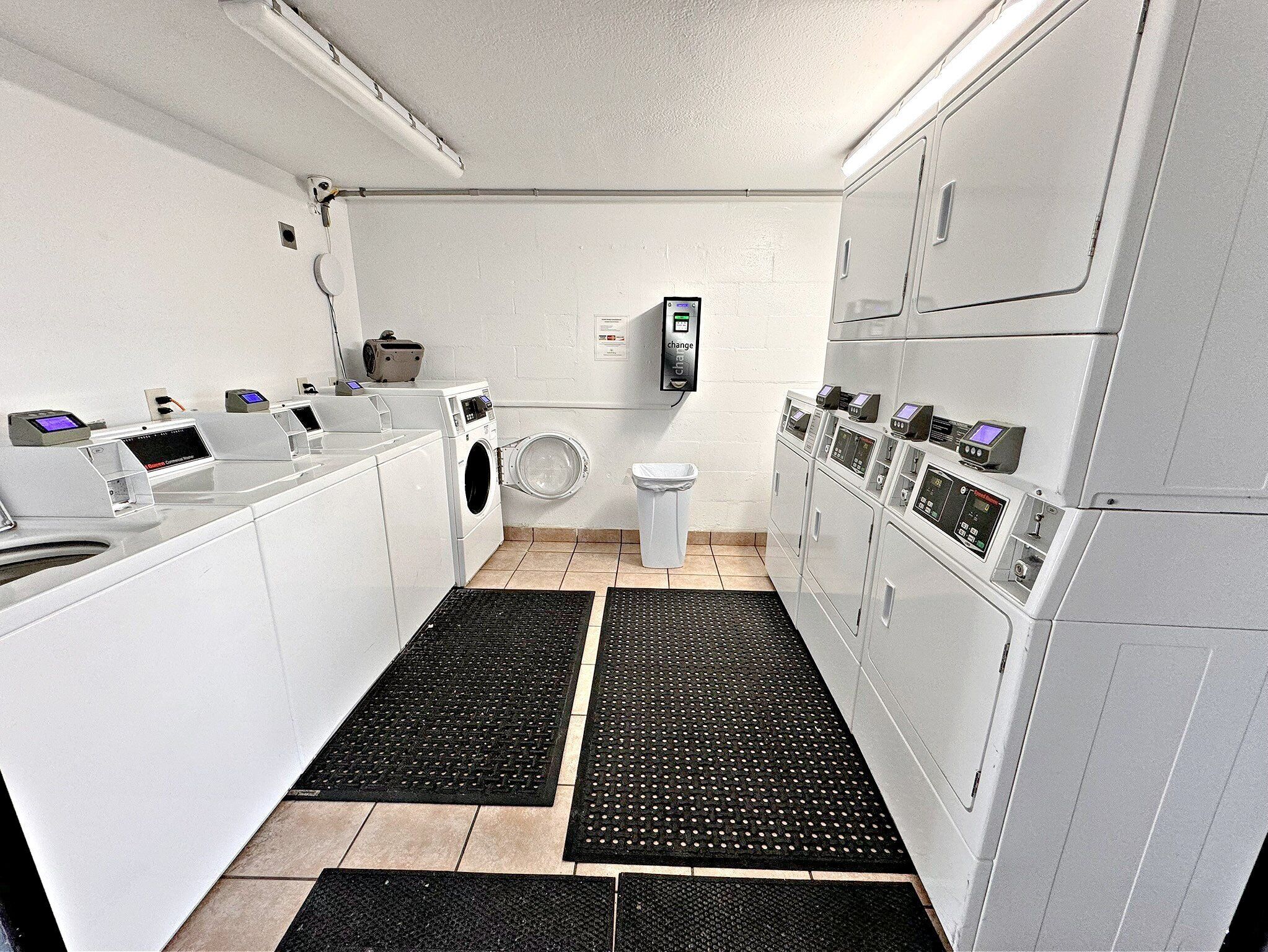 A laundry facility with multiple washing machines and dryers, a toilet, and a control panel.
