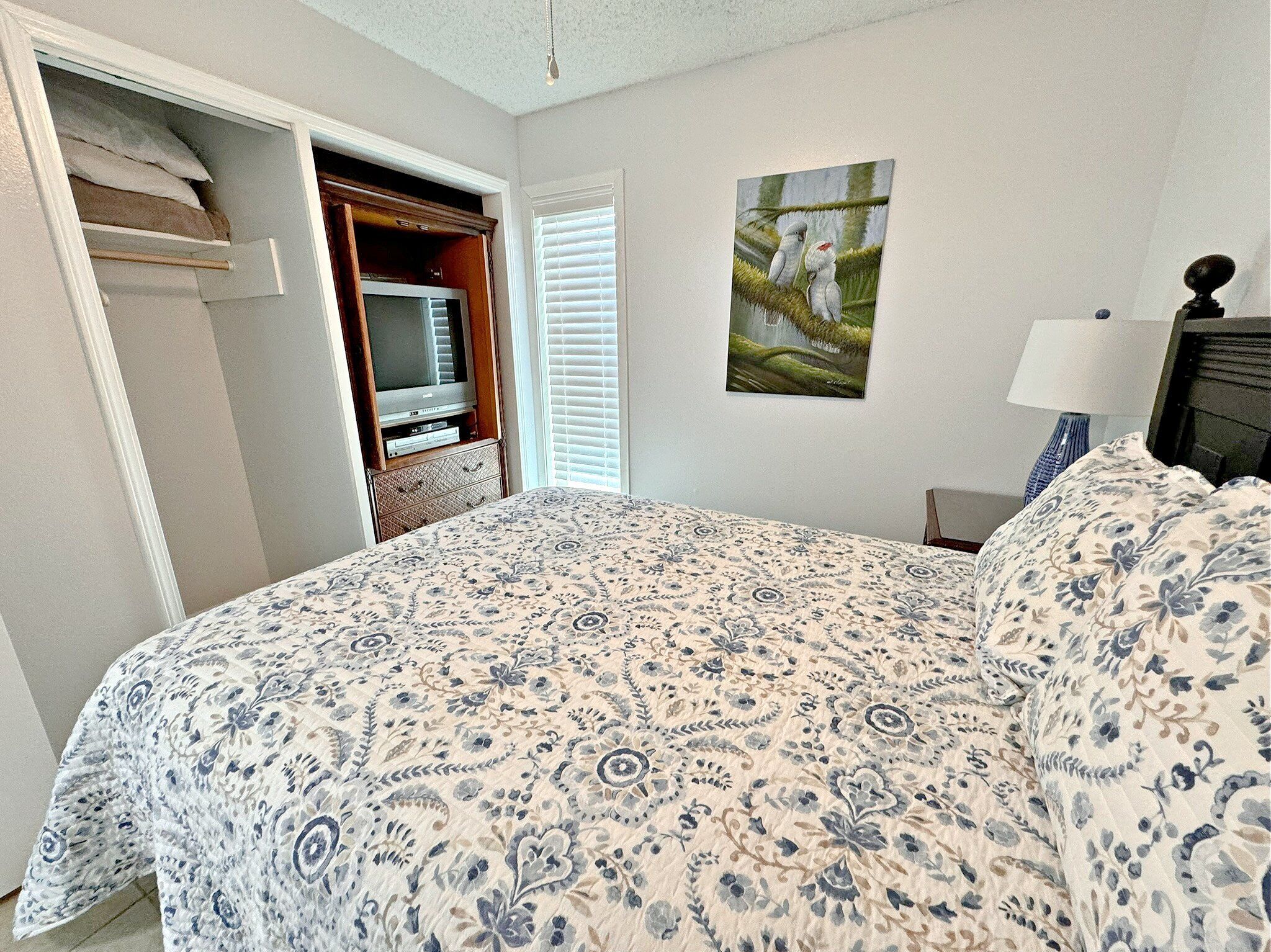 A bedroom with a bed, a television, a painting, and a lamp.