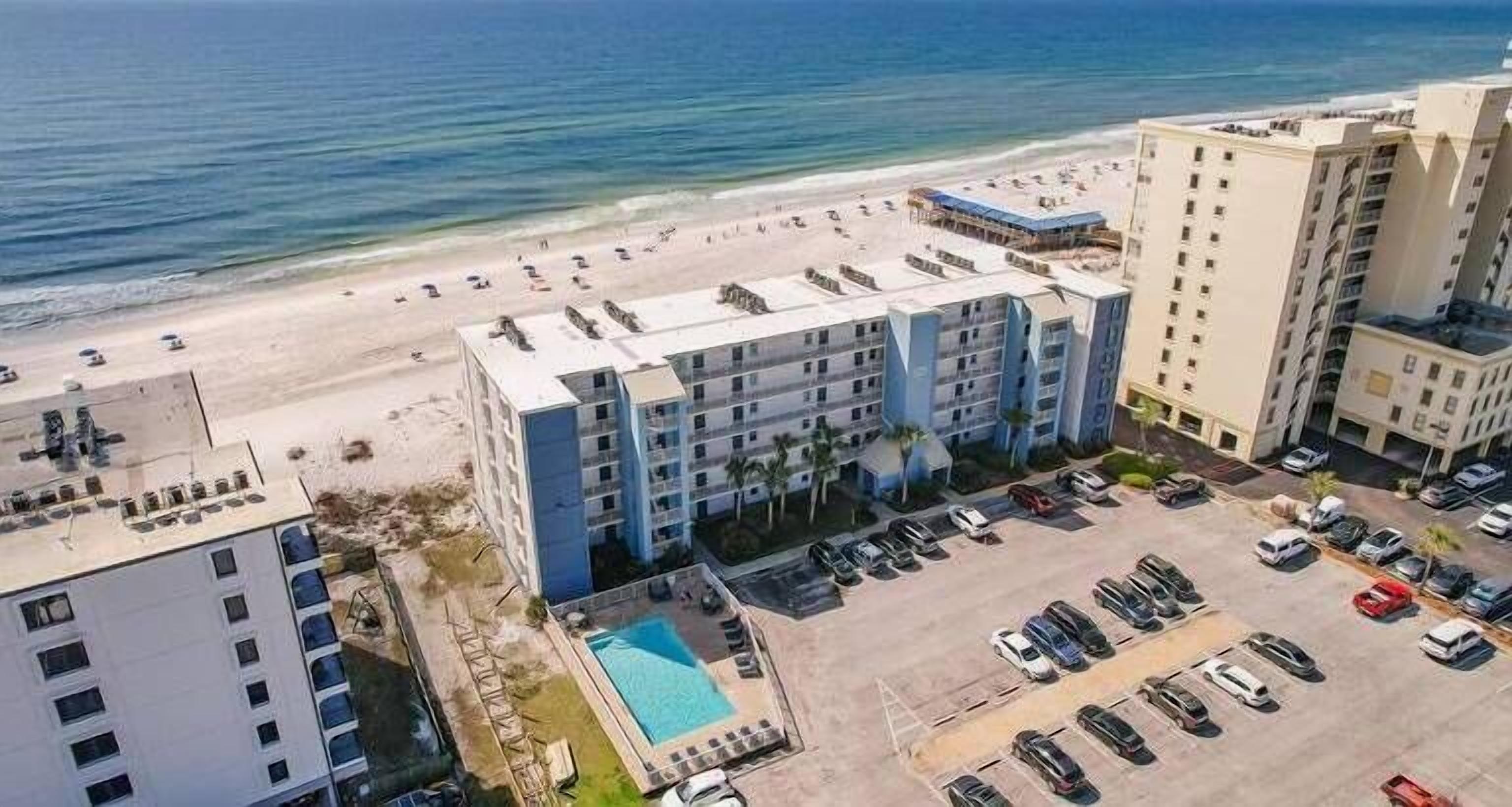 A multi-story hotel with a rooftop pool, adjacent to a beach.
