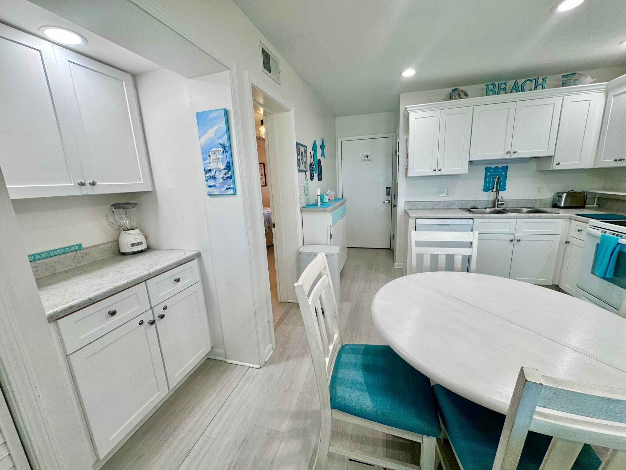 A kitchen with white cabinets, a blender on the counter, and a dining area with a table and chairs.