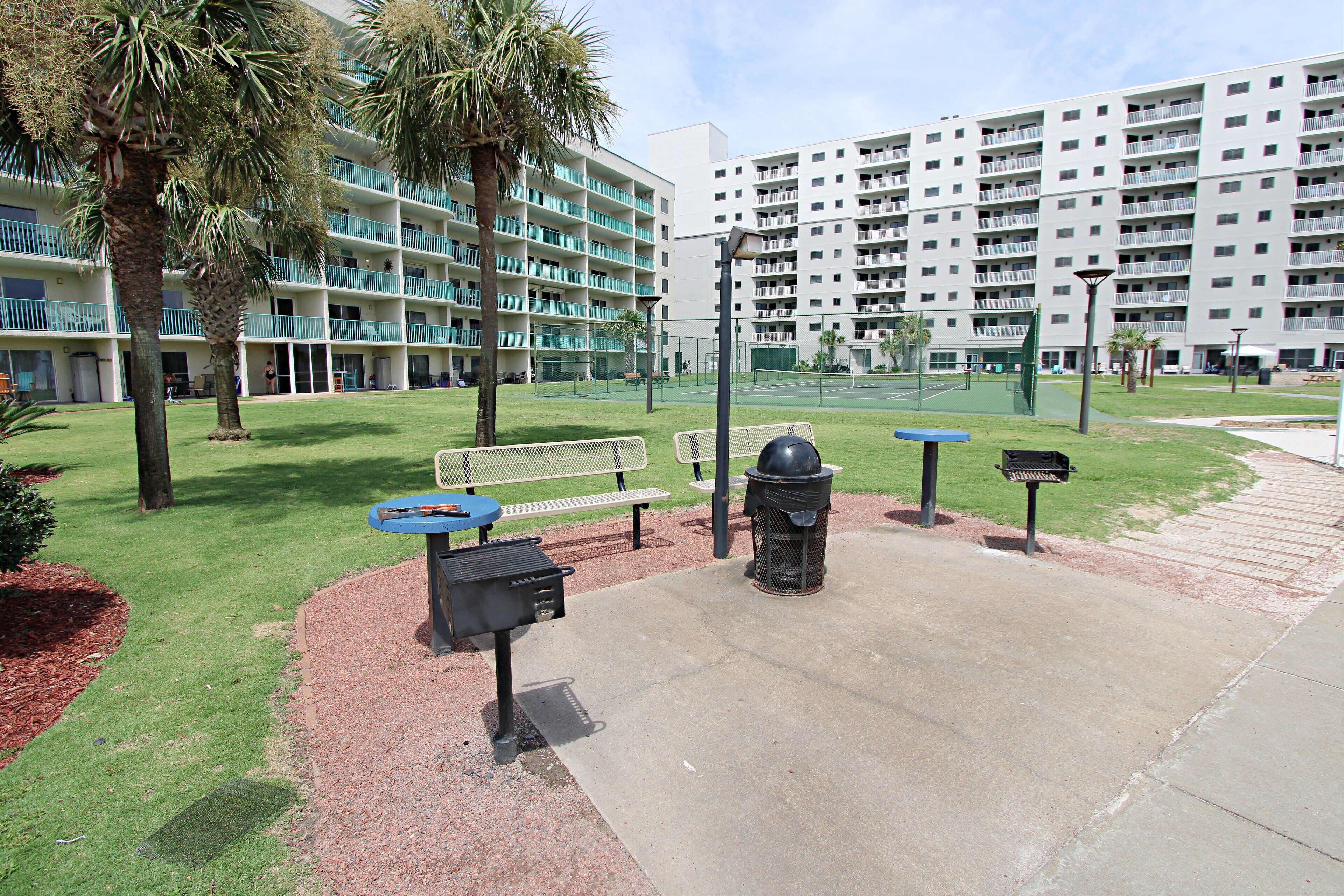 A courtyard with picnic tables, a barbecue grill, and a trash can.
