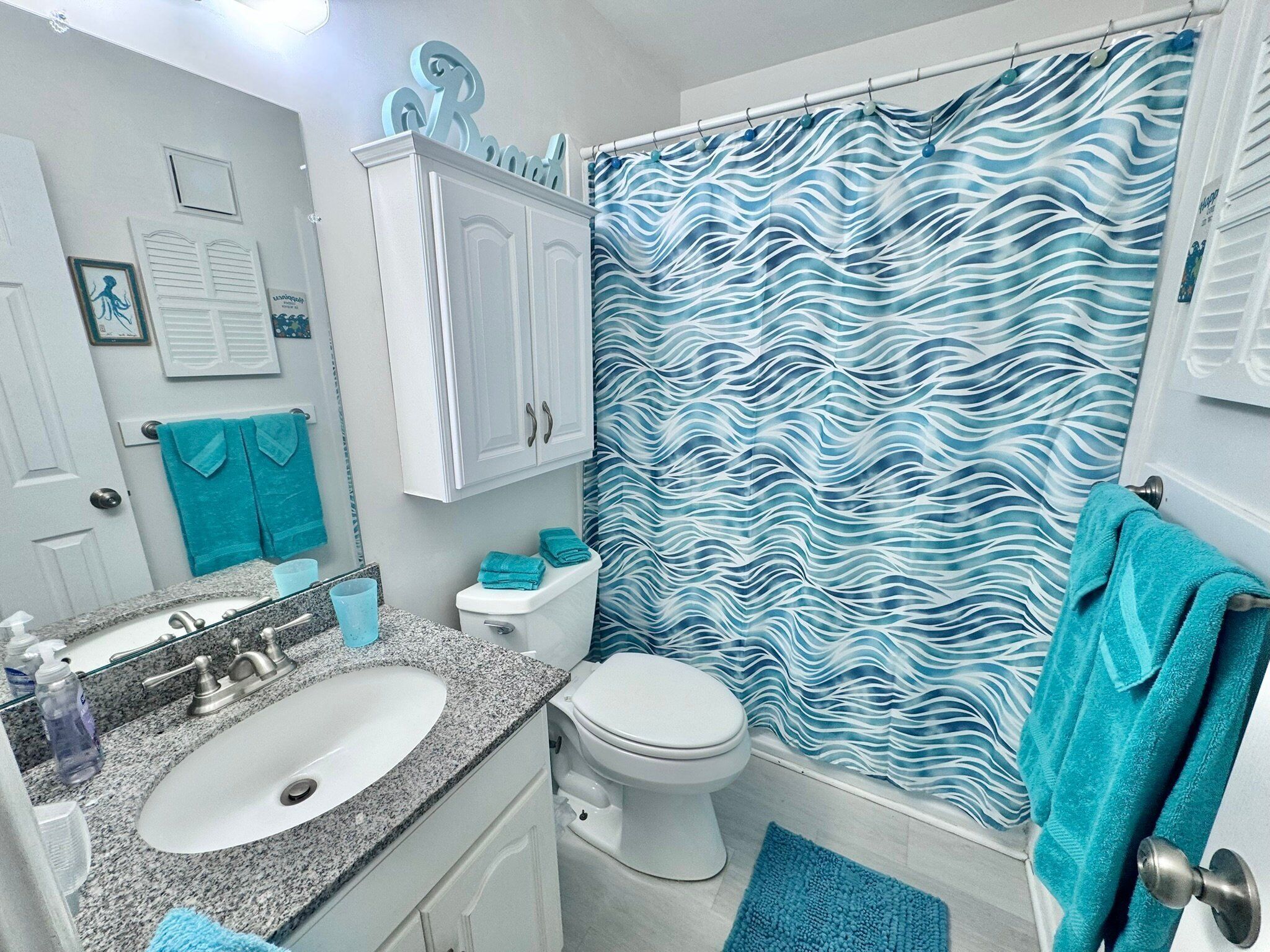 A bathroom with a white sink, a toilet, and a shower curtain with a blue and white wavy pattern.
