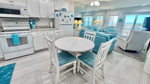 A modern kitchen with white cabinets, a white stove, and a dining area with a white table and blue chairs. - Gulf Shores Plantation (Gulf Shores)