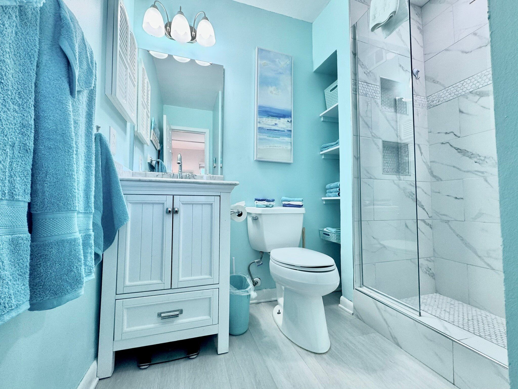 A bathroom with a white vanity, a toilet, a shower with glass doors, and a blue wall.
