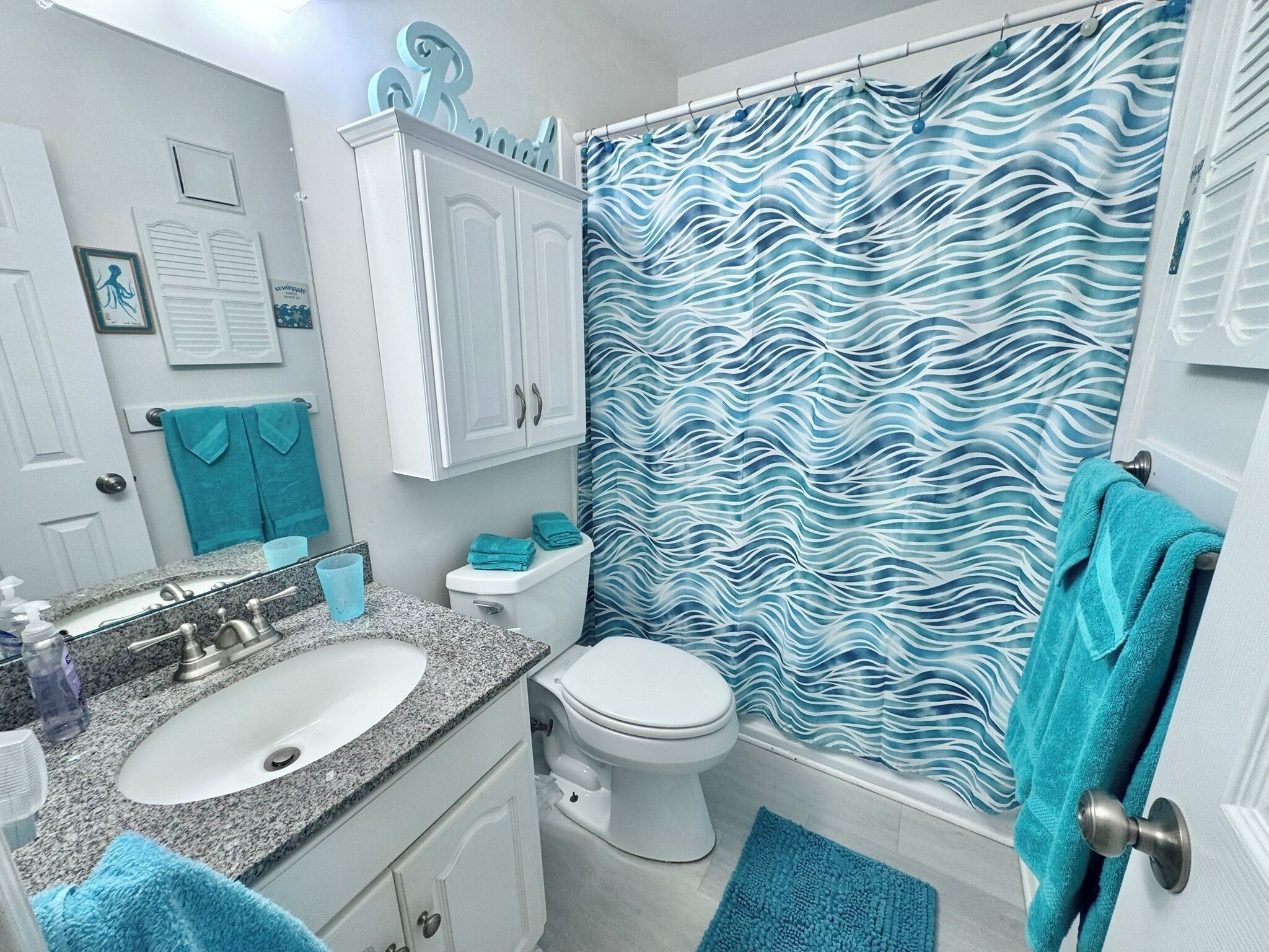 Un bagno con lavandino in granito, WC bianco e tenda da doccia azzurra con decorazioni.