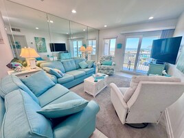 Un salón amplio con un sofá grande, un sillón más pequeño, una mesa de centro y una televisión.