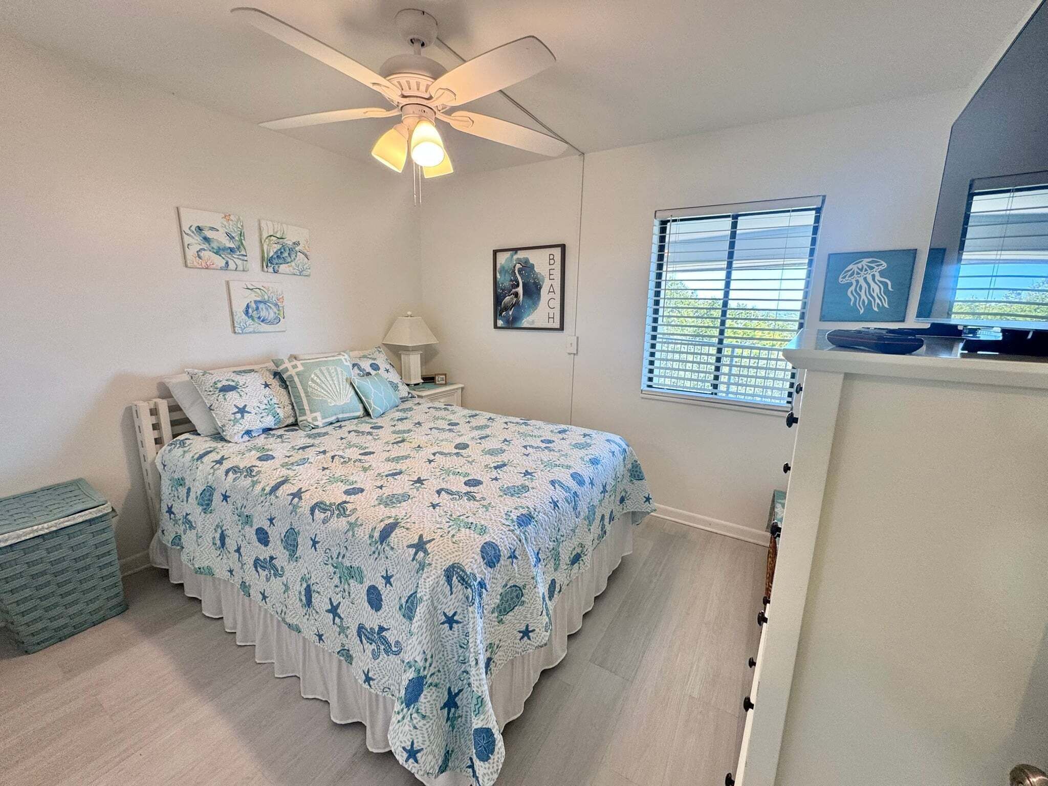 A bedroom with a bed, a ceiling fan, a window with blinds, and wall art.