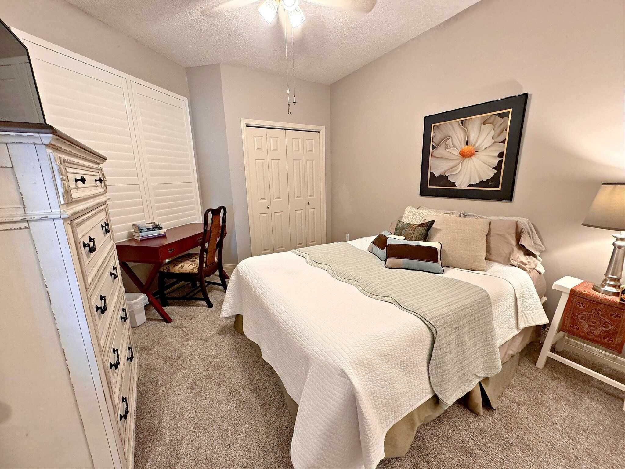 A bedroom with a bed, dresser, desk, chair, and a ceiling fan.