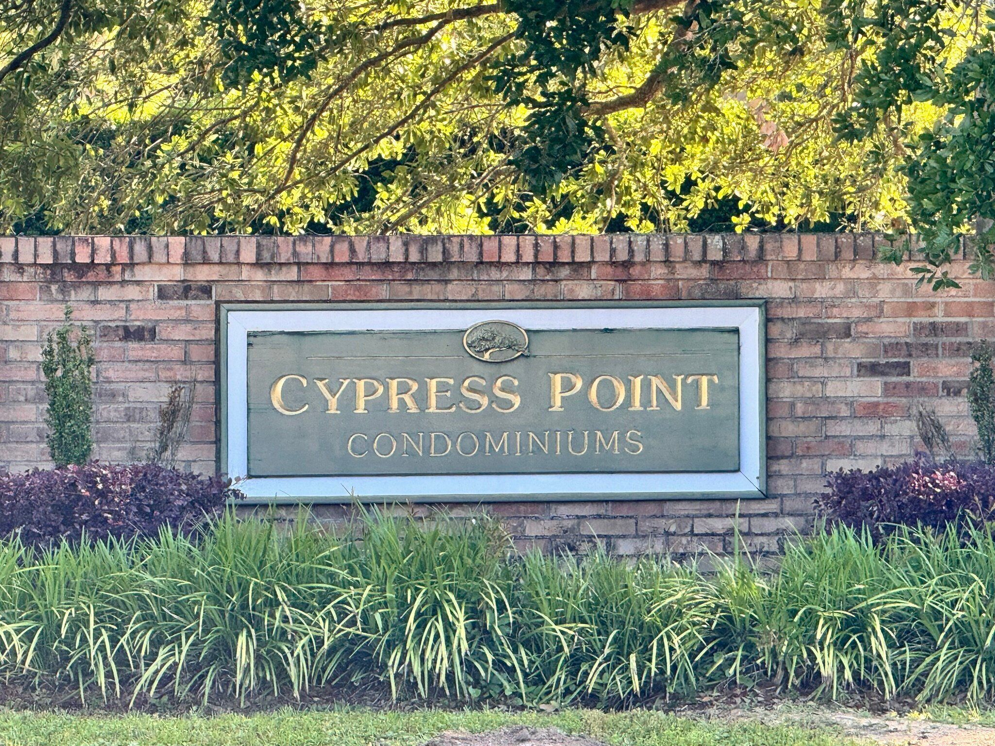 A sign for Cypress Point Condominiums with a brick wall and greenery in the background.