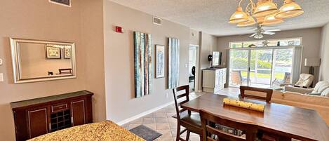 A dining area with a wooden table and chairs, a ceiling fan, and a view of the outdoors through a glass door.