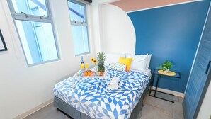 A bedroom with a bed, a small table with a plant, and a window. - Fit for a Queen @ Somos Hotel (San Juan)