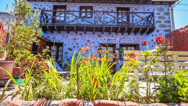 A traditional stone building with a balcony, surrounded by potted plants and flowers.